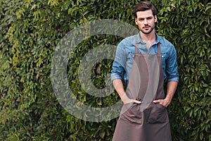 Thoughtful gardener in apron looking at camera while standing in garden