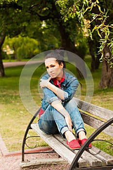 Thoughtful girl with coffee on a bench in the park.