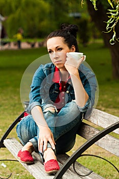 Thoughtful girl with coffee on a bench in the park/