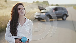 Thoughtful girl with cup in hand looks out at broken car out of city