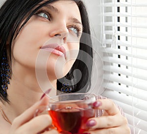 Thoughtful girl drinking tea at the window