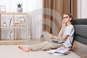 Thoughtful girl with laptop and books on floor at home