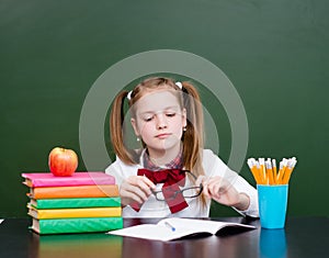 Thoughtful girl looking at her glasses in classroom