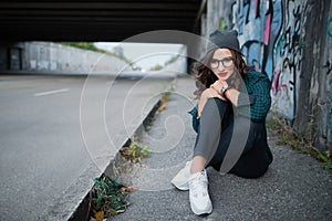 Thoughtful girl sitting on an empty highway under the bridge and thinks