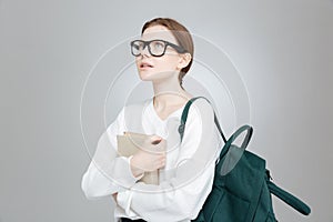 Thoughtful girl student with backpack holding book and thinking