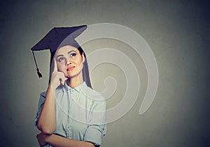 Thoughtful graduate student woman in cap gown looking up thinking