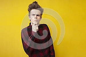 Thoughtful guy with a funny hairstyle puzzled by a choice on a yellow isolated background, hipster student thinks