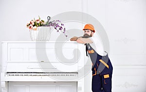 Thoughtful guy leaning on the top of vintage white piano with glass flower vase isolated on white background. Bearded