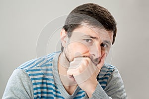 Thoughtful handsome bearded man in a striped sweater leaning his head against his hand looking at the camera