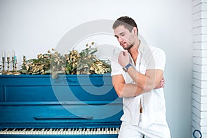 Thoughtful, handsome man with a beard in white clothes against the background of a piano, a rasped shirt with a bare torso