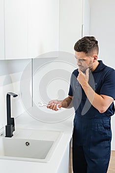 thoughtful handyman holding wrench near sink