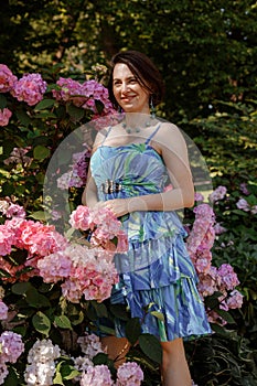 Thoughtful happy young woman surrounded by flowers. Girl throwing rose petals. Gardening and people concept. Woman