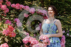 Thoughtful happy young woman surrounded by flowers. Girl throwing rose petals. Gardening and people concept. Woman