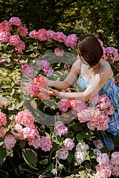 Thoughtful happy young woman surrounded by flowers. Girl throwing rose petals. Gardening and people concept. Woman