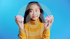 Thoughtful hungry asian woman choosing between donuts