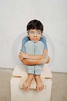 Thoughtful indian boy sitting on a wooden box, hugging his knees.