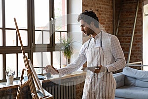 Thoughtful inspired young artist guy drawing at easel