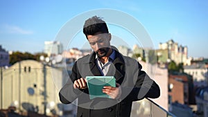 Thoughtful intelligent Middle Eastern man surfing Internet on tablet standing on rooftop at golden sunset. Portrait of