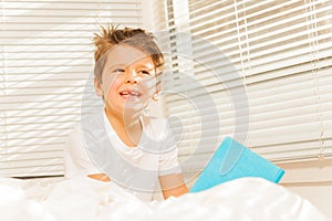 Thoughtful kid boy sitting in his bed with a book