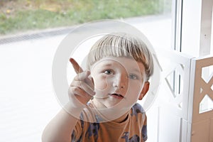 a thoughtful little boy of 3 years at the window looks and he points at something with his index finger