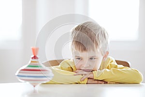 Thoughtful boy sits at the table and looks at the spinning top photo