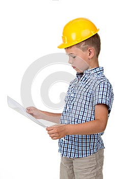 Thoughtful little builder boy in yellow hardhat and checkered shirt holding a paper plan in his hands, isolated on white