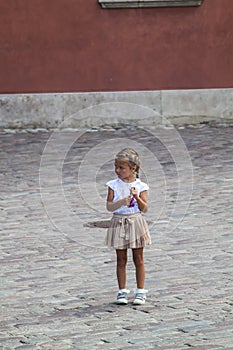 thoughtful little girl standing alone on the pavement in the square