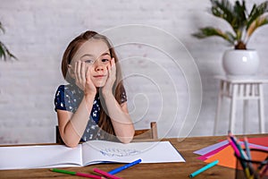 Thoughtful little girl at the table draw with crayons