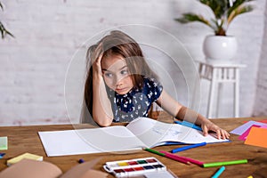 Thoughtful little girl at the table draw with crayons