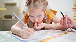 A thoughtful little schoolgirl does her homework, nervous and biting nails