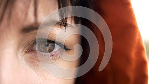 Thoughtful looking young woman eyes brown in contact lenses. In the orange hood on the head. Looking into the camera