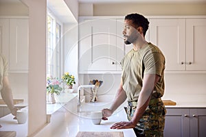 Thoughtful Male American Soldier In Uniform In Kitchen On Home Leave Looking Out Of Window