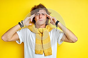 Thoughtful male keeps hand on temple isolated on yellow wall