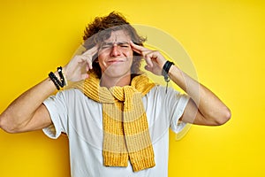 Thoughtful male keeps hand on temple isolated on yellow wall