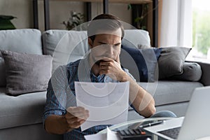 Thoughtful man checking financial documents, calculating bills, using laptop
