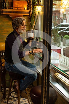 Thoughtful man drinking coffee looking at people passing by.