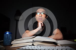 Thoughtful man in glasses studying using books and computer