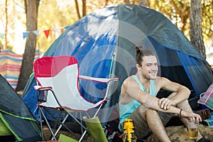 Thoughtful man holding beer glass while sitting at campsite