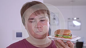 Thoughtful man holds delicious hamburger in kitchen closeup