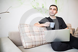 Thoughtful man with laptop and cup of coffee on sofa at home
