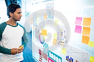 Thoughtful man looking at sticky notes and charts