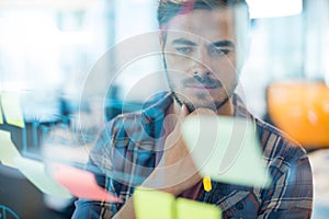 Thoughtful man reading sticky notes on the glass wall