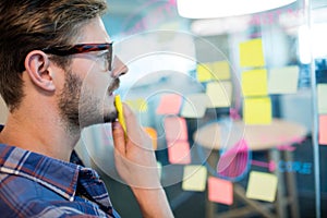 Thoughtful man reading sticky notes on the glass wall