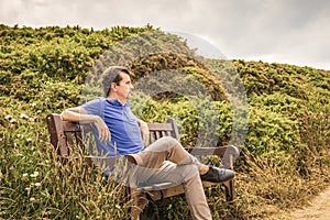 Thoughtful man sitting on a wooden bench in nature