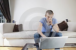 Thoughtful man using laptop while sitting on sofa at home