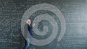 Thoughtful man walking near chalkboard thinking then writing formulas finding solution