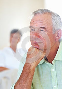 Thoughtful mature man at home with woman in background. Thoughtful mature man thinking in living room with woman in