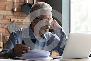 Thoughtful mature man paying bills online on laptop