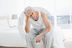 Thoughtful mature man sitting in bed