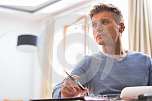 Thoughtful mature man sitting while holding pen at table